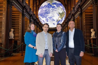 Four people in a library standing in front of an image of the Earth